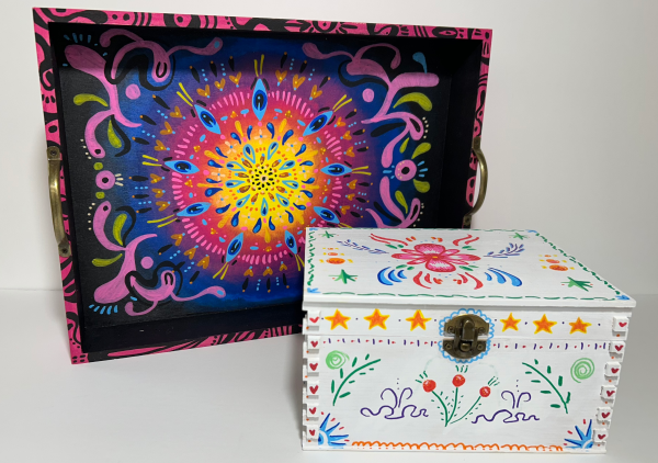 A black tray with colorful abstract designs sits behind a white box with colorful floral illustrations on it