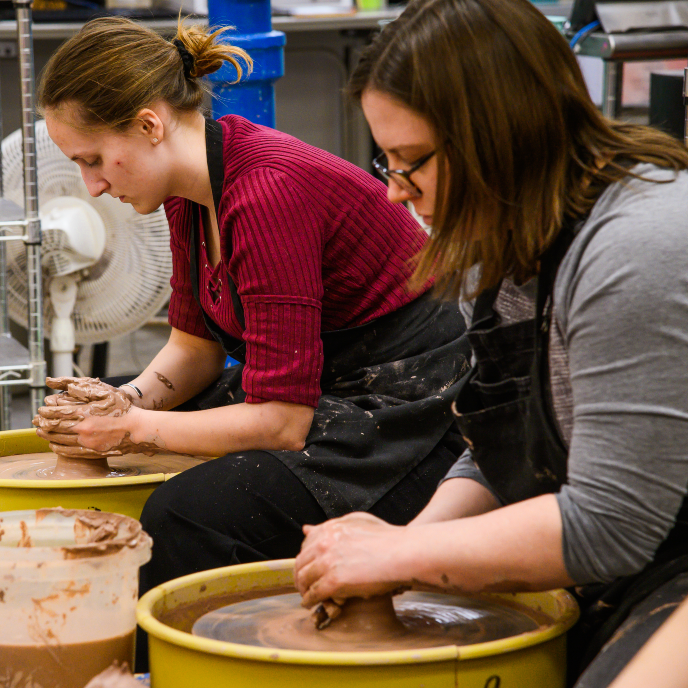 two people at pottery wheels working with clay