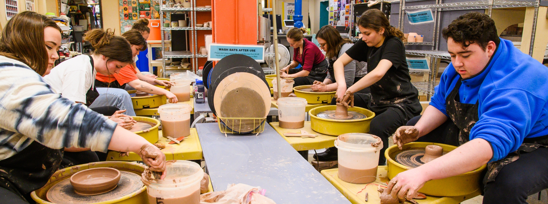 students working at row of pottery wheels in the workspace