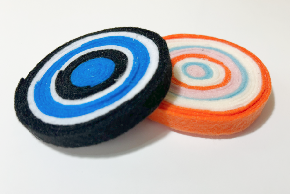 Two coasters made of felt coiled around itself. One is navy blue, royal blue and white; the other is orange, white, light blue and light pink